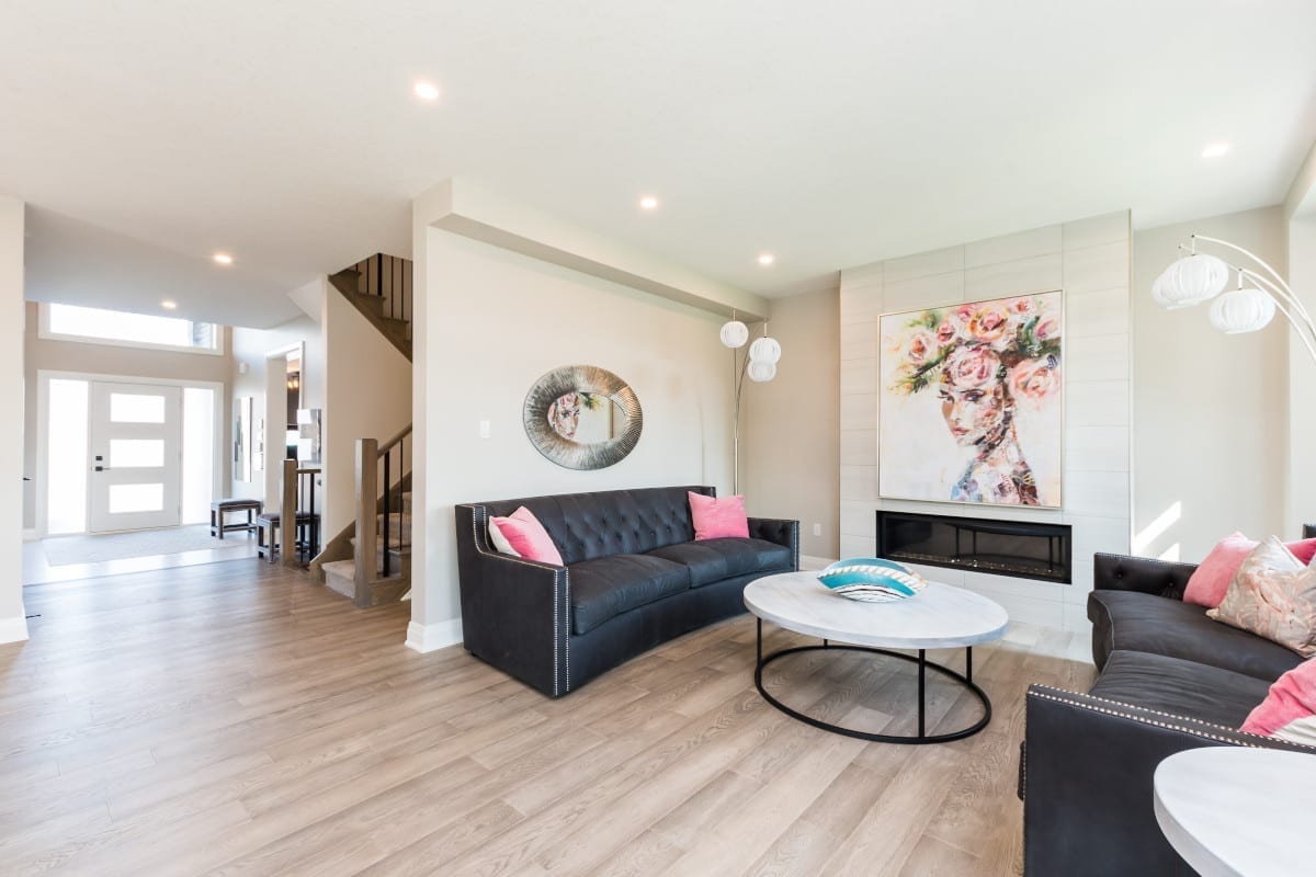 Bright living area with high ceilings styled with dark grey sofas, accented with pink cushions.